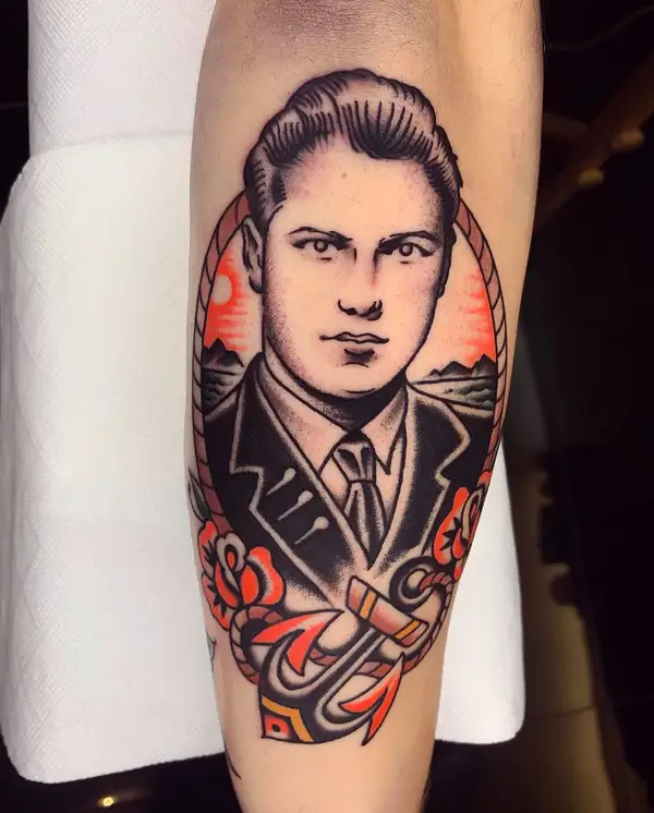 Retrato de un hombre con traje y corbata en tradicional, dentro de un óvalo con el mar, un ancla y flores rojas, en el antebrazo.