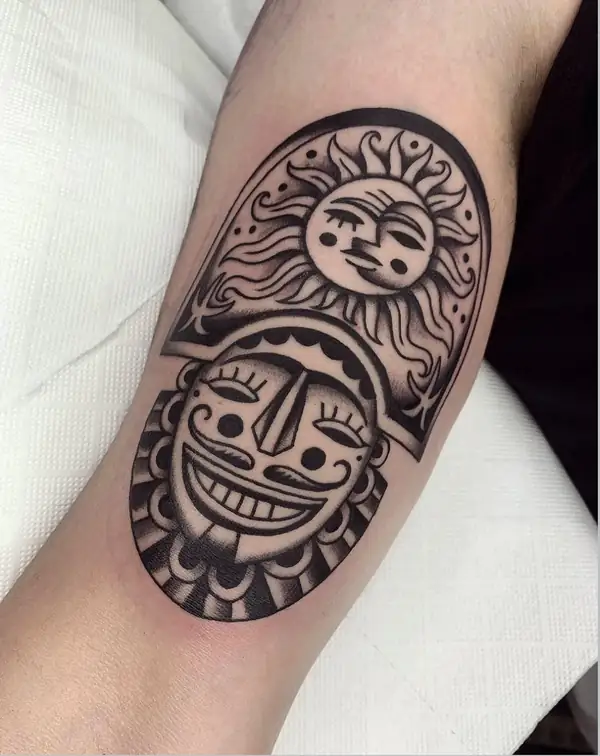 Un sol con cara sobre una máscara sonriente, en tradicional en negro en el brazo.