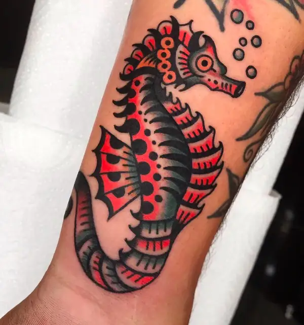 Caballito de mar en rojo y negro, con burbujas, en tradicional en el antebrazo.