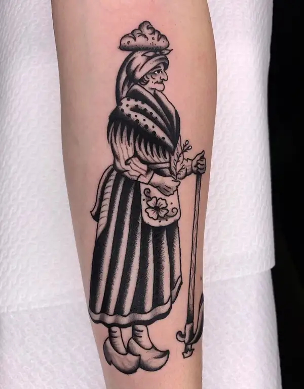 Anciana con pañuelo, mantón y bastón que lleva un fardo en la cabeza, en tradicional en negro en el antebrazo.