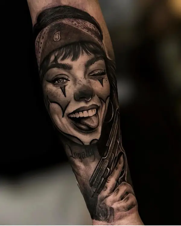 Chica maquillada de payaso que guiña un ojo y saca la lengua, en negro y grises en el antebrazo.