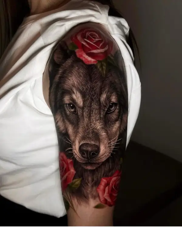 Lobo en negro y grises entre rosas rojas, en el hombro.
