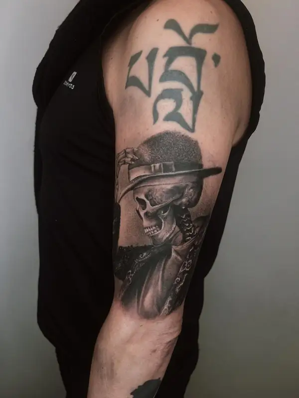 Una calavera con sombrero y chaqueta, en negro y grises en el brazo.