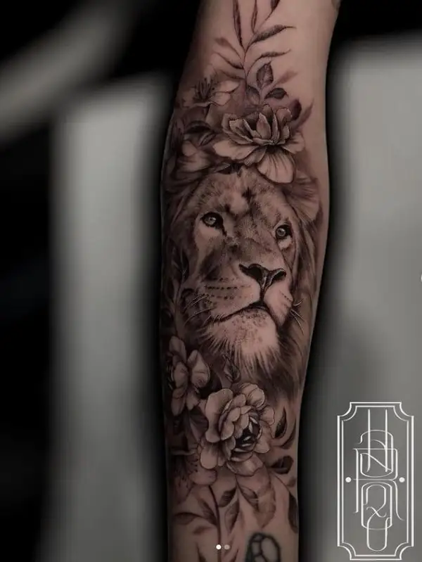 León entre flores, en negro y grises en el antebrazo.
