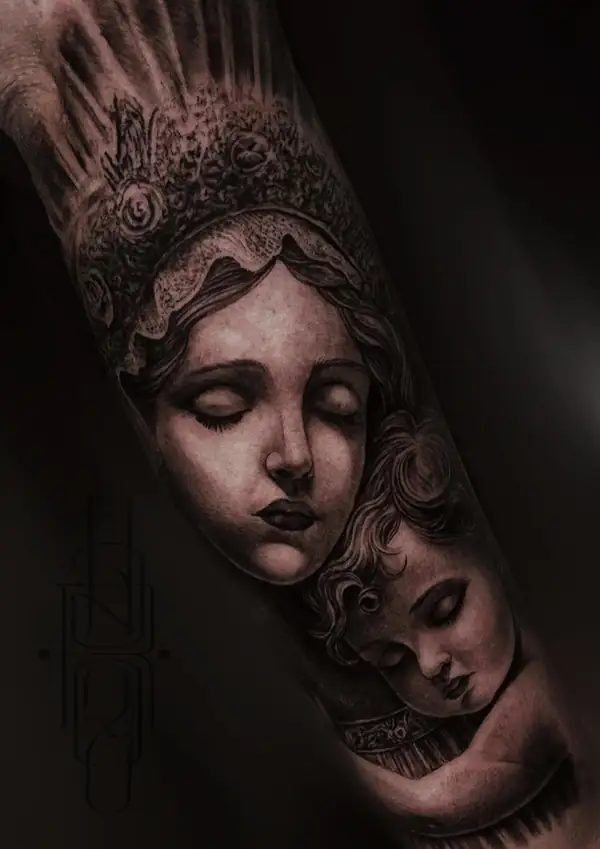 Rostro de mujer con corona y un niño ángel, en negro y grises en el antebrazo.