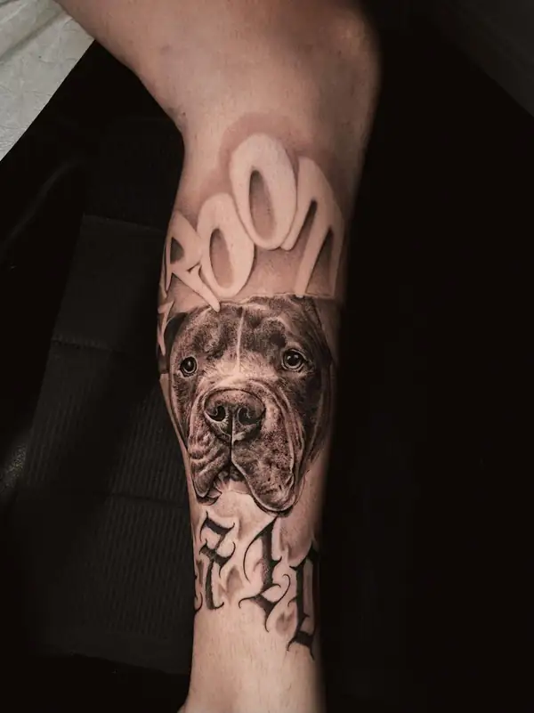 Un perro con su nombre en letras grandes encima, en negro y grises en el antebrazo.