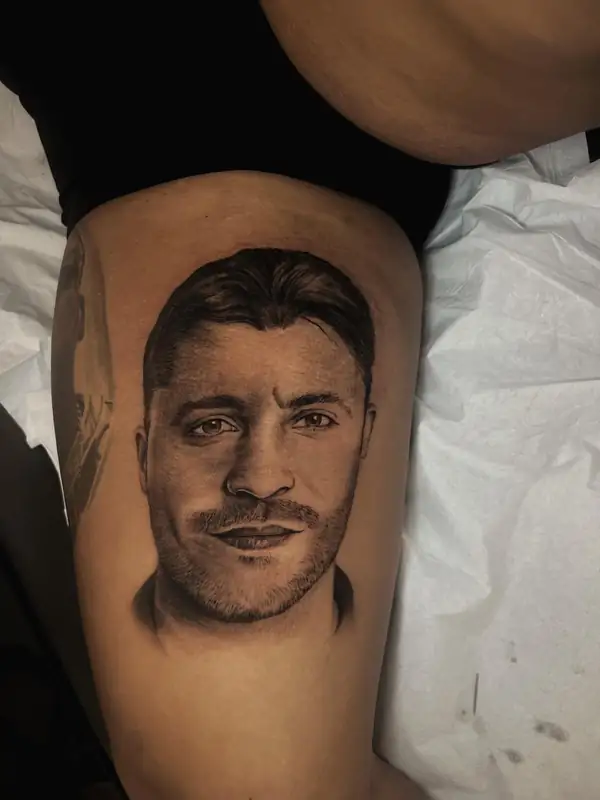 Retrato realista de un hombre sonriendo, en negro y grises en el muslo.