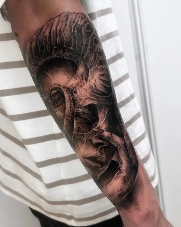Rostros que se entrelazan, en negro y grises en el antebrazo.