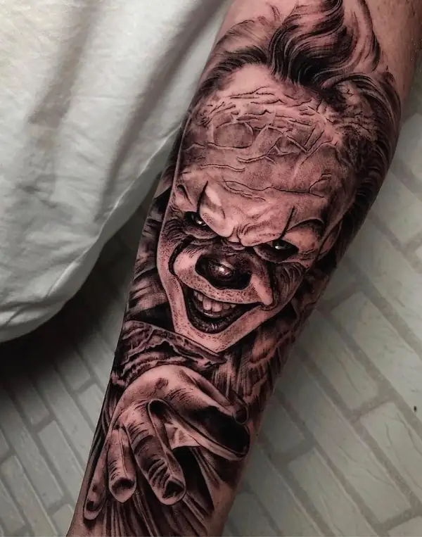 Pennywise, el payaso de «It», sonriendo, en negro y grises en el antebrazo.