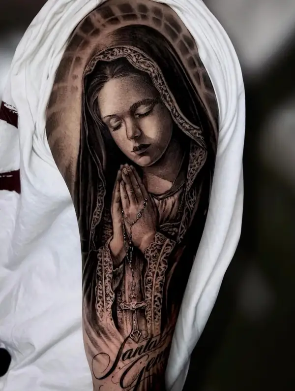 Virgen rezando, con el manto sobre la cabeza y un rosario entre las manos, en negro y grises en el brazo.