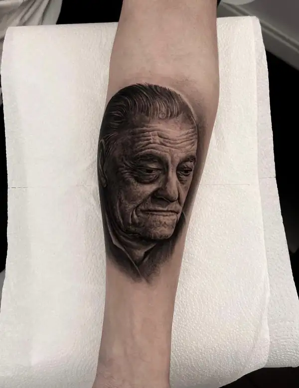 Retrato realista de un hombre mayor en negro y grises en el antebrazo, con las arrugas marcadas a sombra.