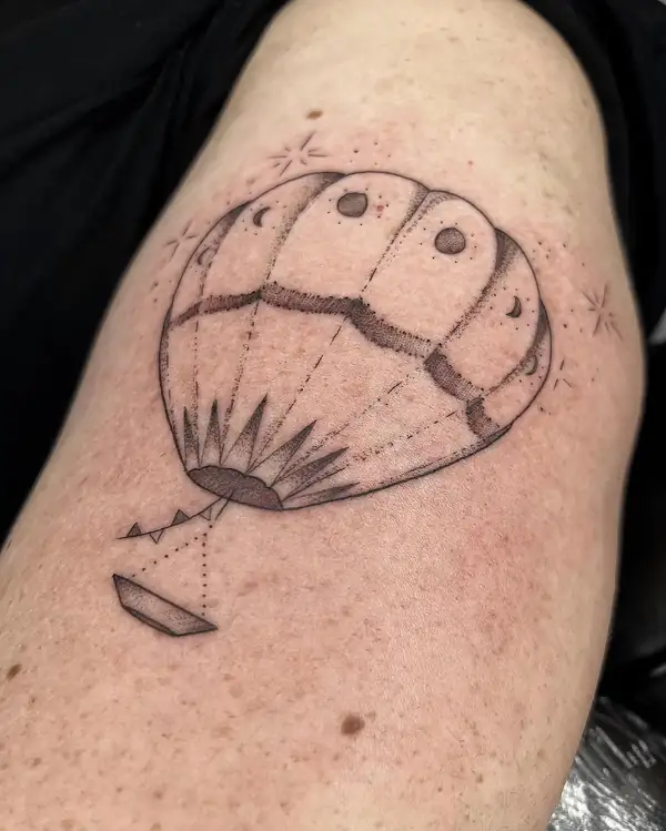 Un globo aerostático con lunas, en línea fina y punteado en el hombro.