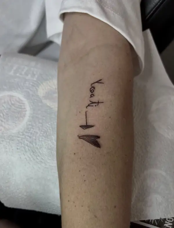 Una palabra en letra fina y dos corazones negros pequeños, en el antebrazo.