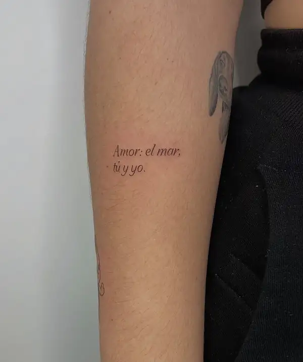 La frase «Amor: el mar, tú y yo.» en letra de máquina en el brazo.