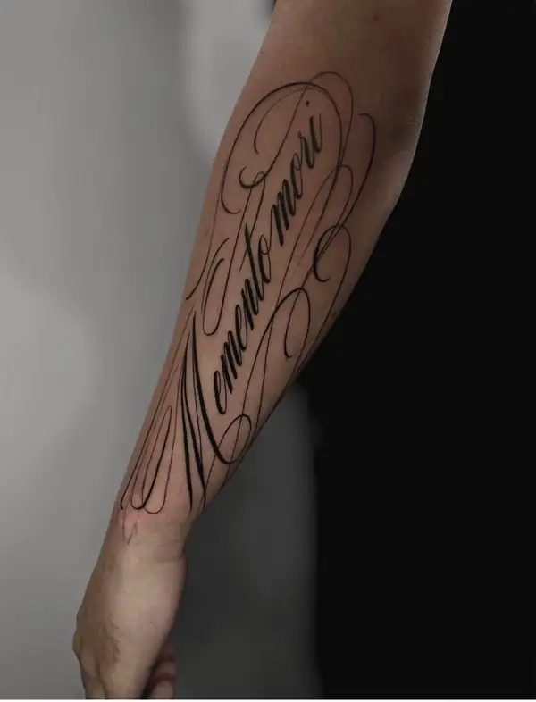 «Memento mori» en letra caligráfica grande a lo largo del antebrazo.