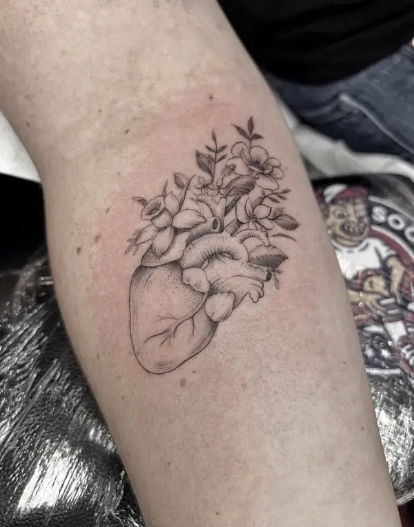 Corazón anatómico del que salen flores, en línea fina y punteado en el antebrazo.