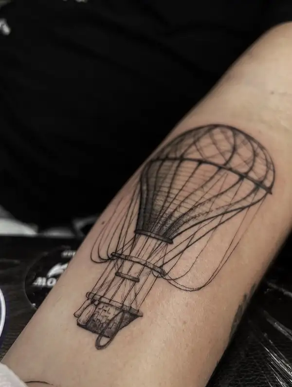 Un globo aerostático en línea fina y punteado en el antebrazo.