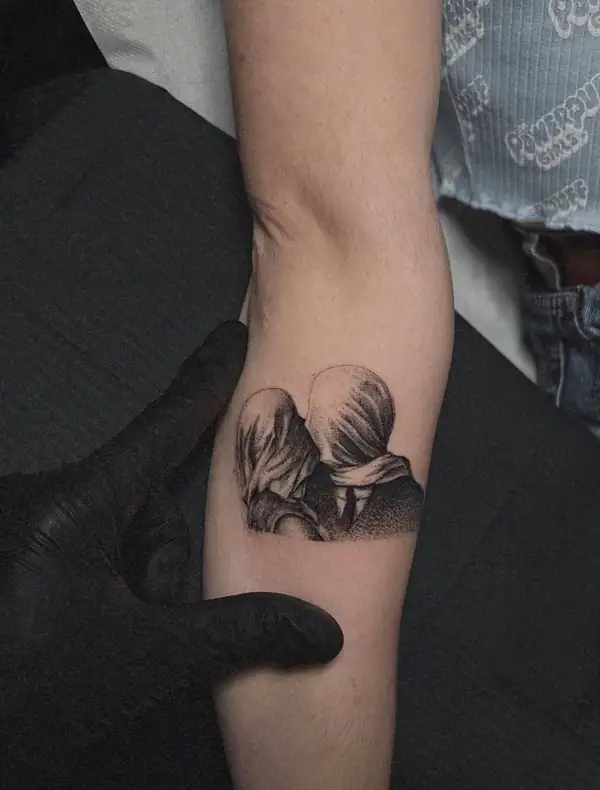 Dos figuras besándose con la cabeza tapada, en puntillismo pequeño en el antebrazo.