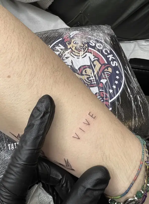 La palabra «VIVE» en letra fina junto a un pajarito, en el tobillo.