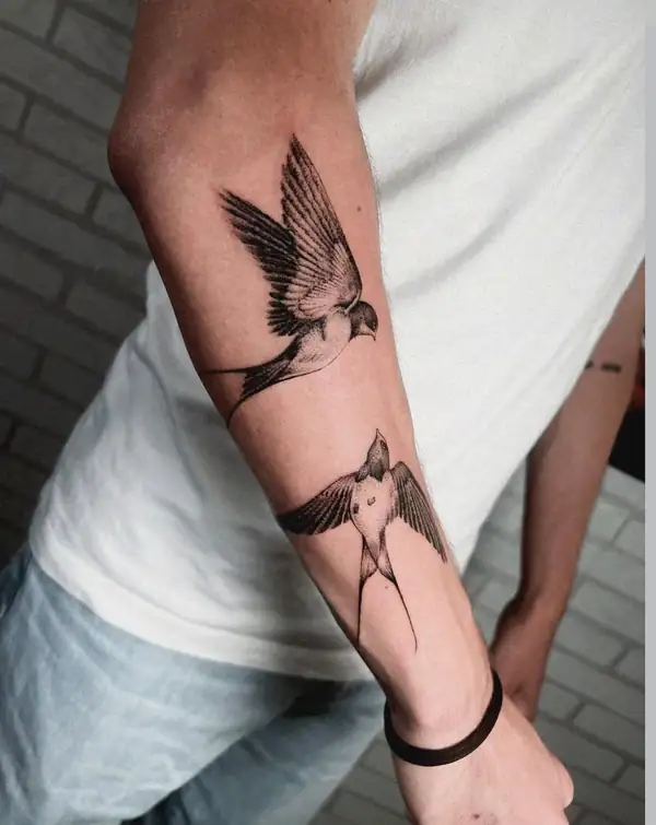 Dos golondrinas en vuelo, en línea fina y punteado en el antebrazo.