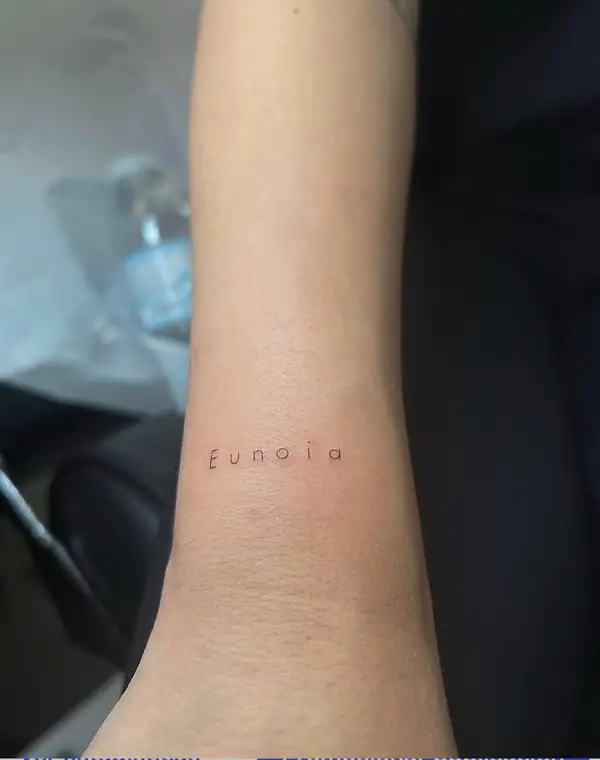 La palabra «Eunoia» en letra fina en el antebrazo.