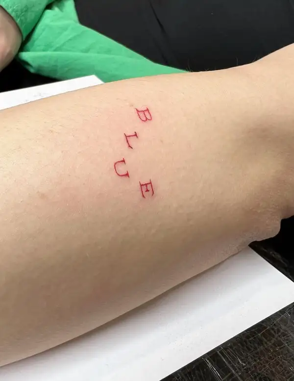La palabra «BLUE» en letras rojas, de arriba abajo, en el antebrazo.
