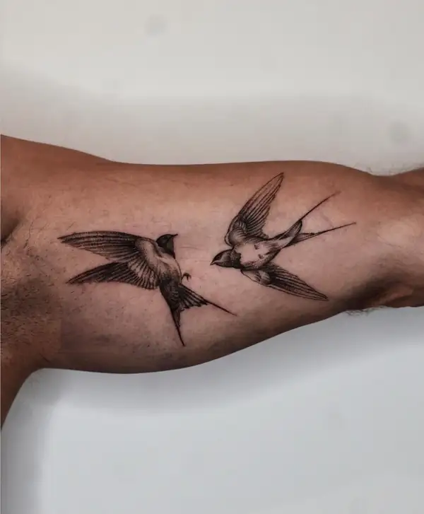 Dos golondrinas frente a frente, en línea fina y punteado en el antebrazo.