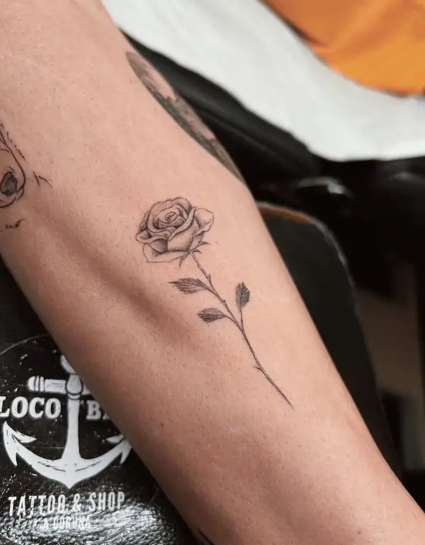 Una rosa de tallo largo en línea fina en el antebrazo.