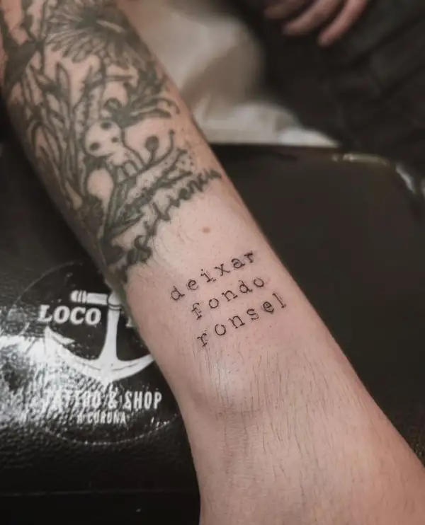 La frase en gallego «deixar fondo ronsel» en letra de máquina en el antebrazo.