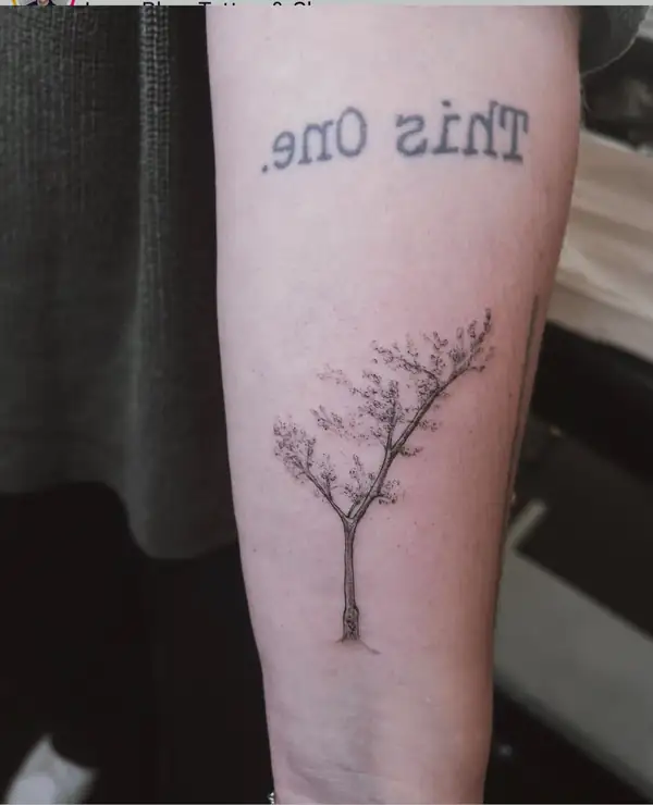 Un árbol en línea fina con la frase «This one.» encima, en el antebrazo.
