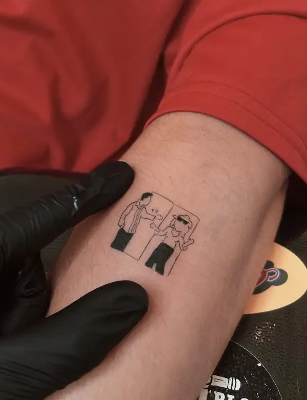 Dos figuras pequeñas en negro, como una viñeta de cómic, en el antebrazo.