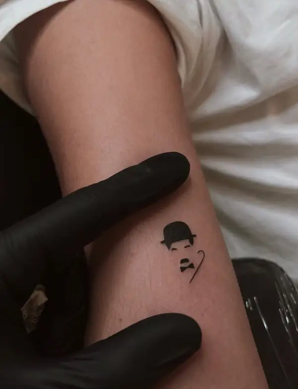 Charlot, con su bombín y su bigote, pequeño y en negro, en el brazo.