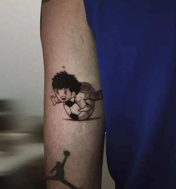 Oliver, de «Oliver y Benji», con el balón, en puntillismo en el antebrazo, con el logo de Jordan debajo.