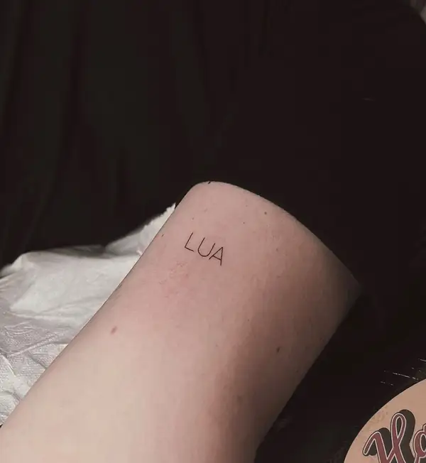 La palabra «LUA» en mayúsculas finas en el brazo.