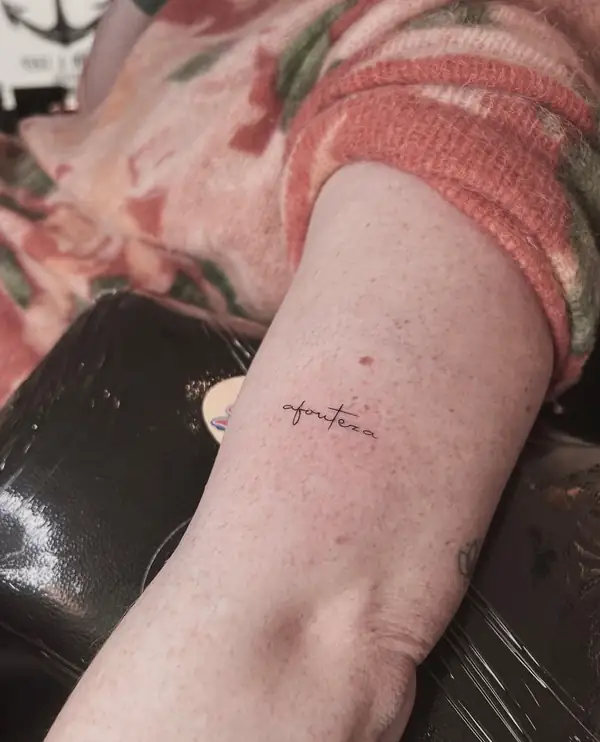 Una palabra en letra cursiva fina en el brazo.