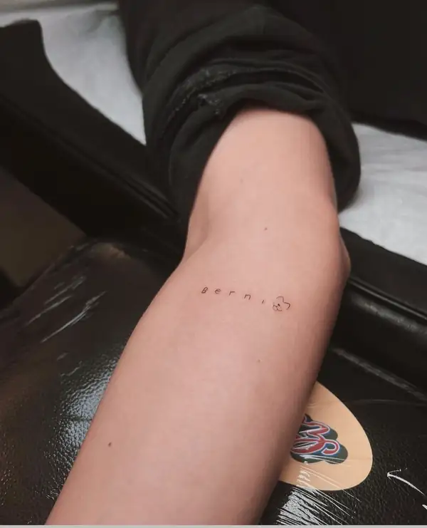 Una palabra en letras separadas y una florecita, en el brazo.