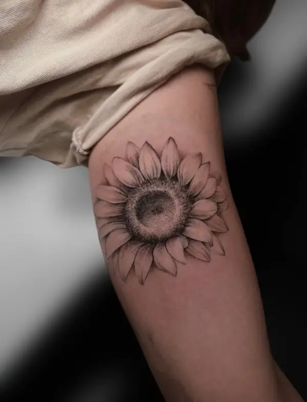 Girasol en línea fina y sombra suave en el brazo.