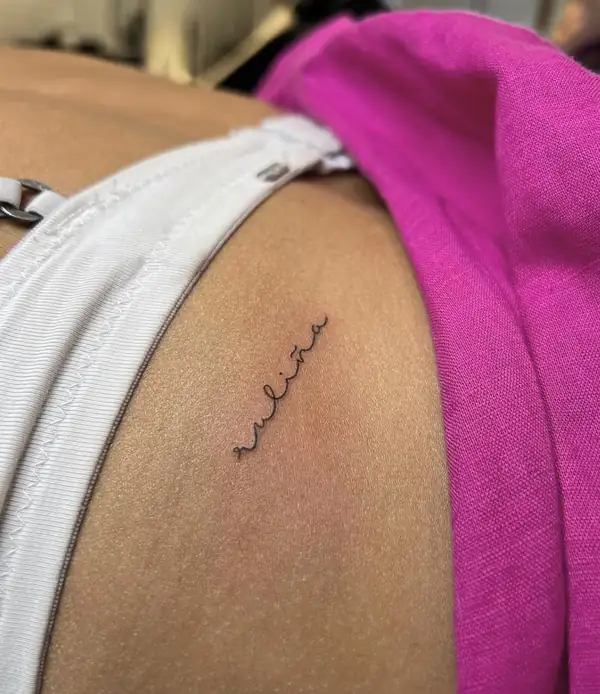 Un nombre pequeño en letra cursiva fina en la cadera.