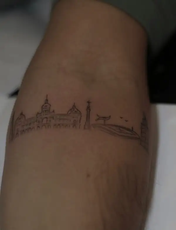 La silueta de una ciudad, con sus cúpulas y torres, en línea fina alrededor del brazo.