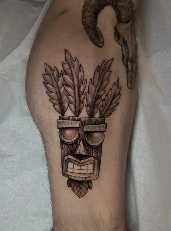 La máscara Aku Aku de Crash Bandicoot, con sus plumas, en puntillismo en la pierna.