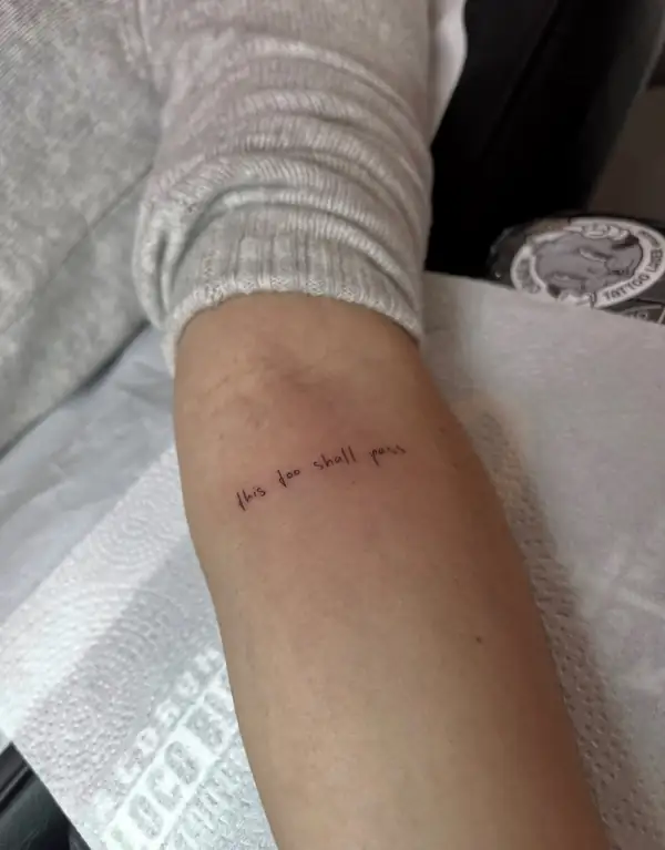 La frase «this too shall pass» en letra fina en el antebrazo.