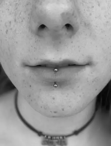 Labret vertical: una barra que sale por el borde del labio de abajo y por debajo de él, en blanco y negro.
