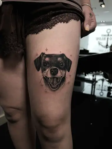 Retrato de una perrita sonriendo, en negro y grises, en el muslo.